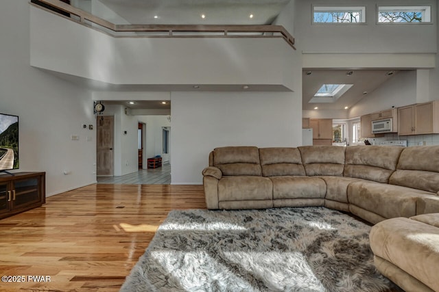 living room featuring a healthy amount of sunlight, a towering ceiling, light hardwood / wood-style flooring, and a skylight