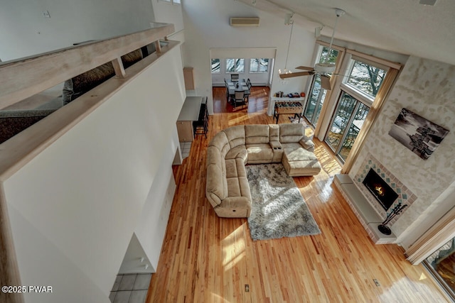 living room featuring a towering ceiling, a fireplace, a wall mounted AC, ceiling fan, and light hardwood / wood-style flooring