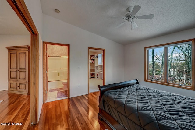 bedroom featuring connected bathroom, a walk in closet, wood-type flooring, vaulted ceiling, and a closet