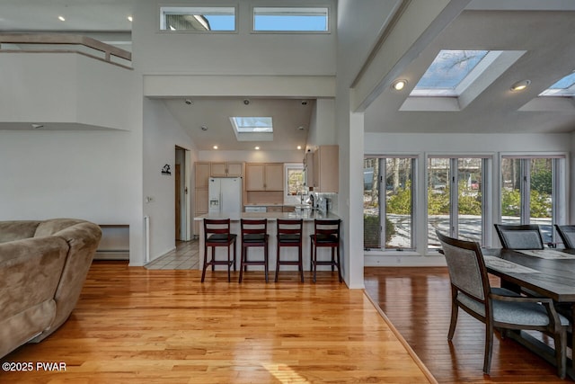 dining room featuring a baseboard heating unit, light wood-type flooring, high vaulted ceiling, and a skylight