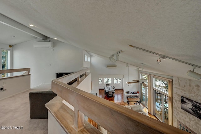 stairway featuring vaulted ceiling with beams, a wall mounted AC, a textured ceiling, track lighting, and carpet flooring