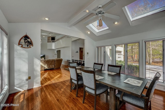 dining room with ceiling fan, hardwood / wood-style flooring, and vaulted ceiling with skylight