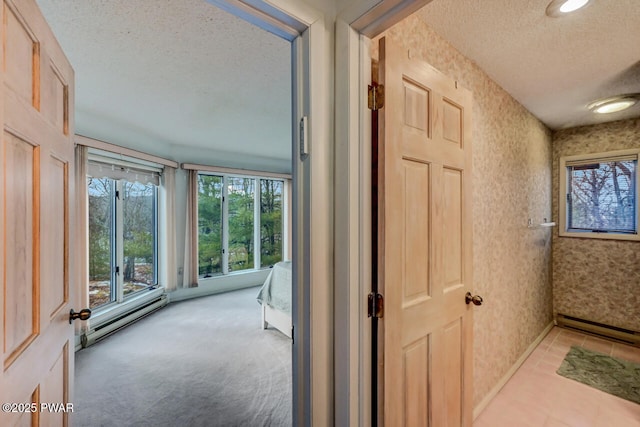 hallway featuring plenty of natural light, light colored carpet, a textured ceiling, and baseboard heating