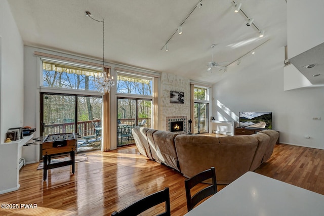 living room with a fireplace, ceiling fan with notable chandelier, light hardwood / wood-style flooring, and high vaulted ceiling