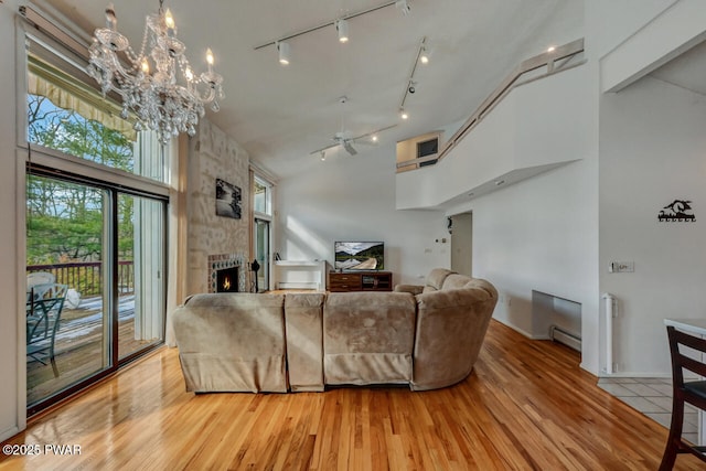 living room featuring a baseboard radiator, wood-type flooring, a stone fireplace, and high vaulted ceiling