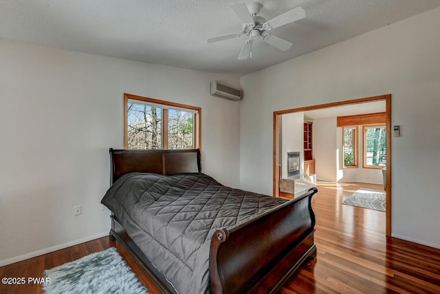 bedroom featuring wood-type flooring, a wall mounted AC, ceiling fan, and a textured ceiling