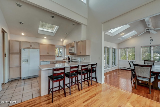 kitchen with white appliances, a skylight, a kitchen breakfast bar, kitchen peninsula, and light brown cabinets