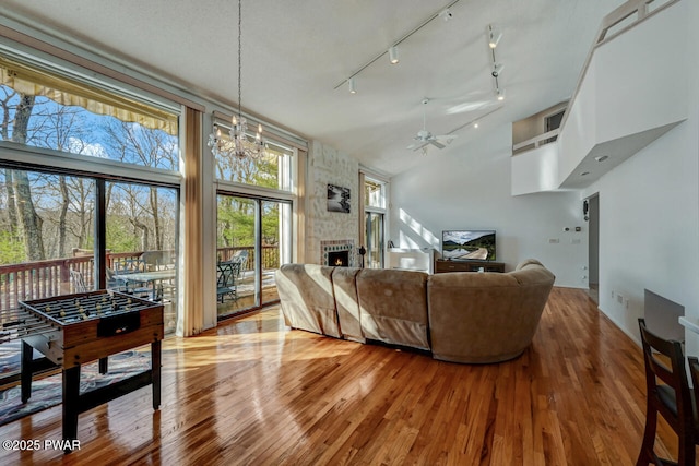 living room with ceiling fan with notable chandelier, a large fireplace, a high ceiling, and light wood-type flooring