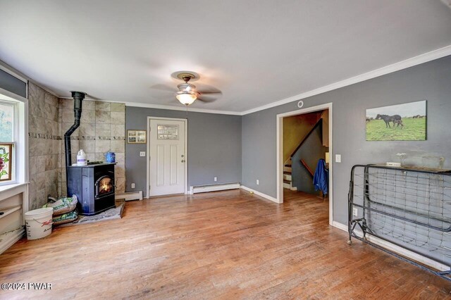 living room featuring hardwood / wood-style floors, a wood stove, a baseboard heating unit, crown molding, and ceiling fan