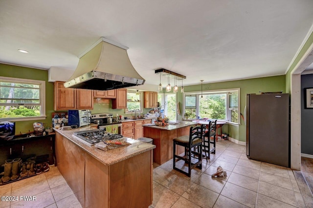 kitchen featuring pendant lighting, light tile patterned floors, appliances with stainless steel finishes, kitchen peninsula, and island exhaust hood