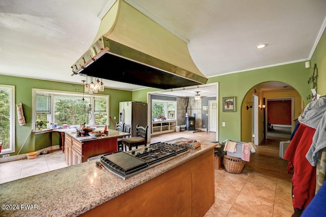 kitchen with island exhaust hood, stainless steel appliances, a center island, a wood stove, and light tile patterned flooring