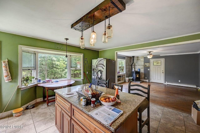 kitchen with a wood stove, a baseboard heating unit, hanging light fixtures, stone countertops, and stainless steel refrigerator