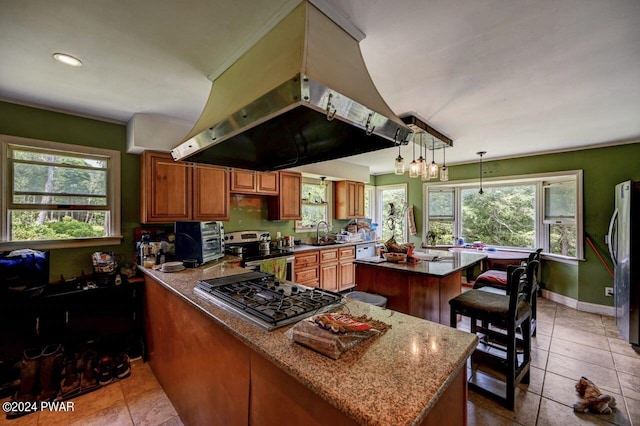 kitchen with island exhaust hood, appliances with stainless steel finishes, sink, decorative light fixtures, and a center island