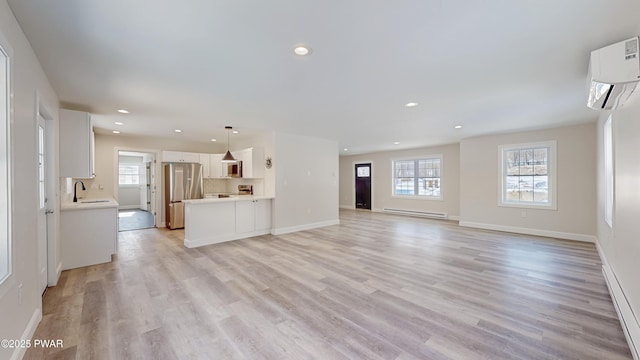 unfurnished living room featuring a baseboard heating unit, sink, a wall mounted AC, and light wood-type flooring