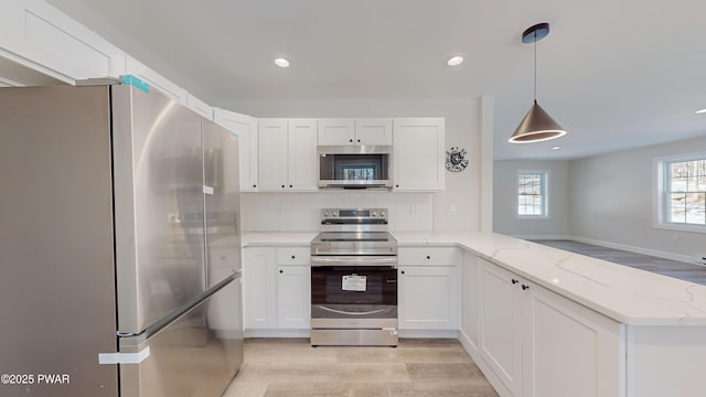 kitchen featuring white cabinetry, light stone counters, kitchen peninsula, pendant lighting, and stainless steel appliances