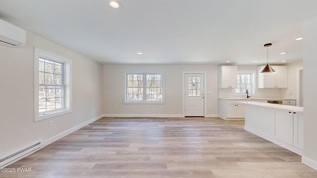 unfurnished living room with an AC wall unit, a baseboard heating unit, sink, and light hardwood / wood-style floors