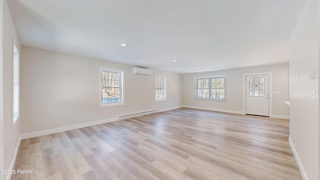 spare room with a baseboard heating unit, a wall unit AC, and light hardwood / wood-style flooring