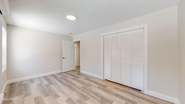 unfurnished bedroom featuring a wall mounted AC, light hardwood / wood-style floors, and a closet