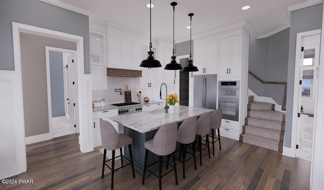 kitchen featuring white cabinetry, hanging light fixtures, light stone counters, a kitchen island with sink, and ornamental molding