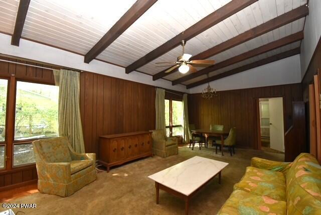 living room featuring lofted ceiling with beams, wood walls, carpet floors, and ceiling fan with notable chandelier