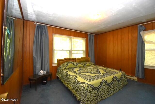 carpeted bedroom featuring multiple windows, wooden walls, and a baseboard radiator