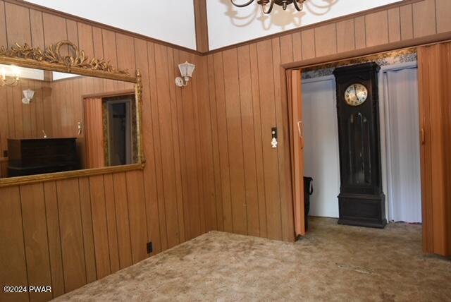 interior space with carpet flooring, wood walls, and an inviting chandelier