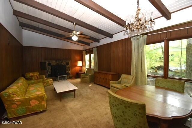 carpeted living room with vaulted ceiling with beams, wood walls, ceiling fan with notable chandelier, and a fireplace