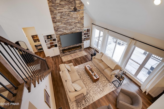 living area featuring dark wood-style flooring, a stone fireplace, a high ceiling, and stairs