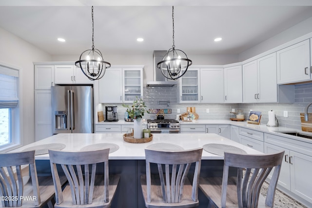 kitchen with a center island, stainless steel appliances, decorative backsplash, a sink, and wall chimney range hood