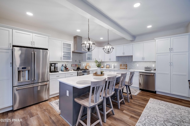 kitchen with high end appliances, dark wood-type flooring, white cabinets, a sink, and wall chimney range hood