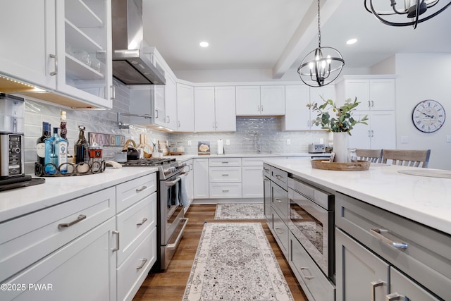 kitchen featuring wall chimney exhaust hood, glass insert cabinets, light stone countertops, stainless steel appliances, and backsplash