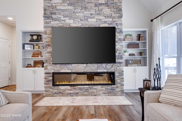 living area featuring wood finished floors, vaulted ceiling, a wealth of natural light, and a stone fireplace