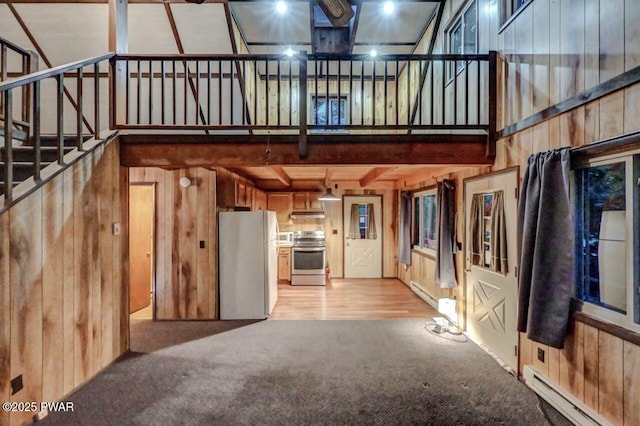 169 Boulder Rd, Lake Ariel, PA 18436 - unfurnished living room with a baseboard radiator, a high ceiling, wood walls, light carpet, and stairway