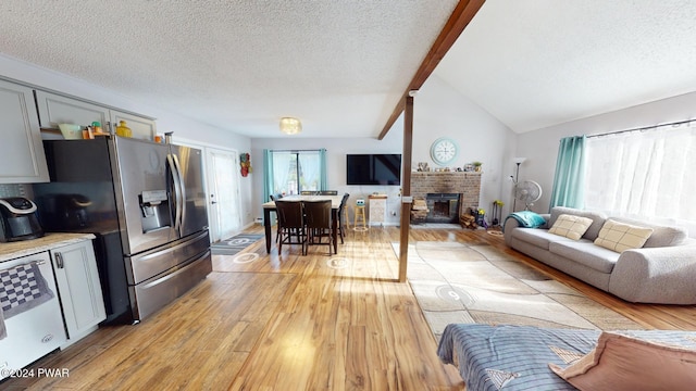 living room featuring a textured ceiling, vaulted ceiling with beams, light wood-type flooring, and a fireplace