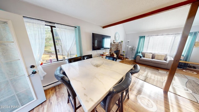 dining space featuring plenty of natural light, lofted ceiling with beams, a baseboard radiator, and light wood-type flooring