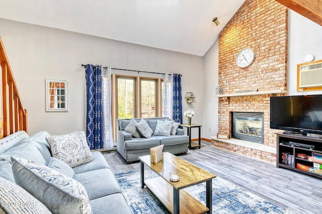 living room with a wall unit AC, light wood-type flooring, high vaulted ceiling, and a brick fireplace