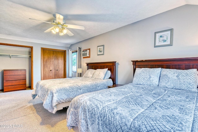 carpeted bedroom with a textured ceiling, two closets, vaulted ceiling, and ceiling fan