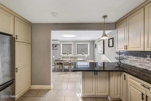 kitchen with pendant lighting, stainless steel refrigerator, dark stone countertops, decorative backsplash, and cream cabinets