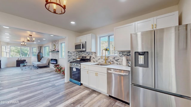 kitchen with stainless steel appliances, sink, an inviting chandelier, white cabinetry, and hanging light fixtures