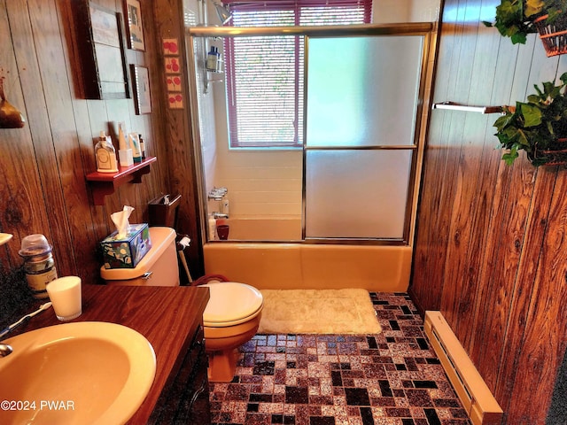 full bath featuring wooden walls, toilet, baseboard heating, combined bath / shower with glass door, and a sink