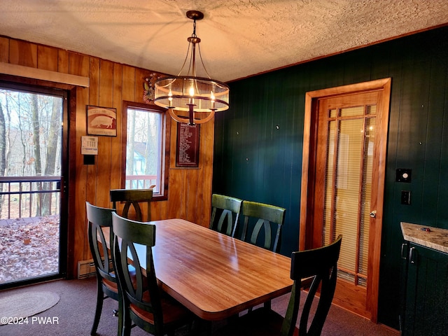 dining area featuring an inviting chandelier, wood walls, a textured ceiling, a baseboard heating unit, and carpet flooring