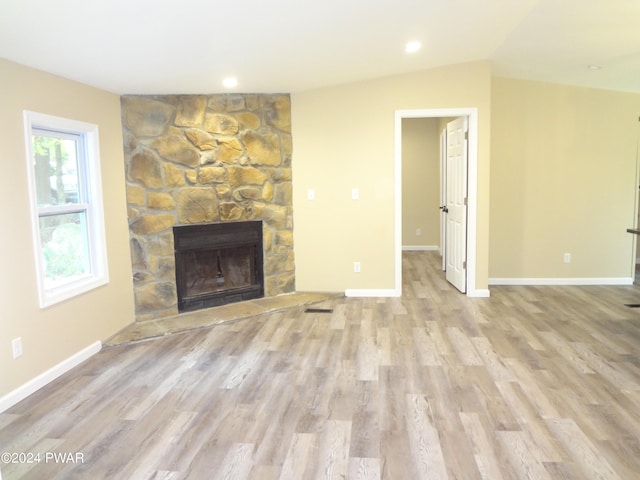 unfurnished living room featuring baseboards, a fireplace, lofted ceiling, and light wood-style floors