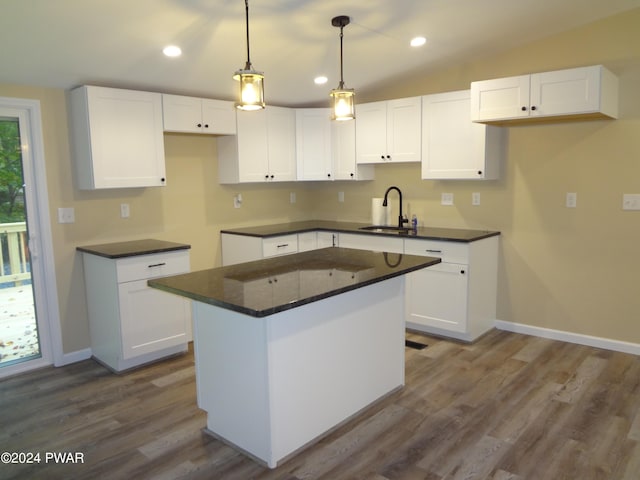 kitchen with dark countertops, vaulted ceiling, white cabinets, and a sink