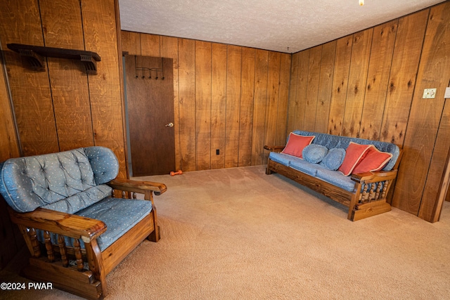 sitting room with wooden walls, light carpet, and a textured ceiling