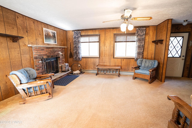 living room featuring light carpet, wooden walls, ceiling fan, a fireplace, and a textured ceiling