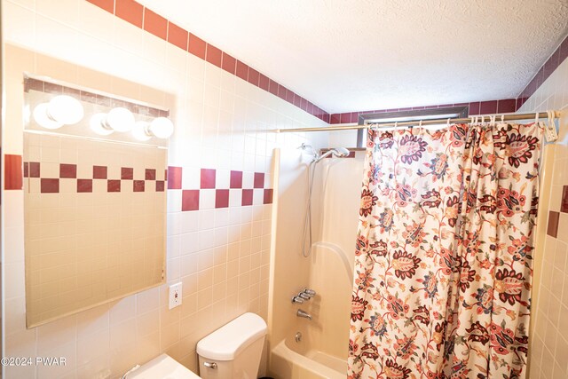 bathroom with a textured ceiling, shower / bath combination with curtain, toilet, and tile walls