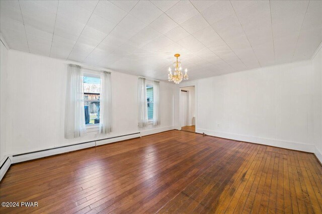 empty room featuring hardwood / wood-style floors, a notable chandelier, and a baseboard heating unit