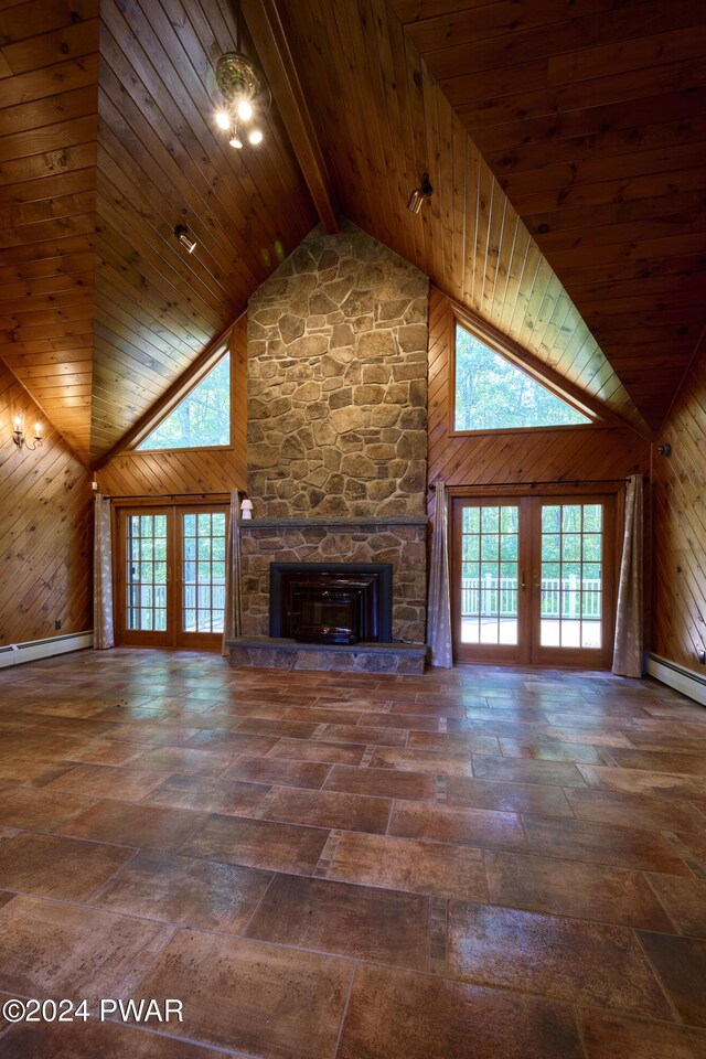 unfurnished living room featuring a stone fireplace, wood walls, french doors, and high vaulted ceiling