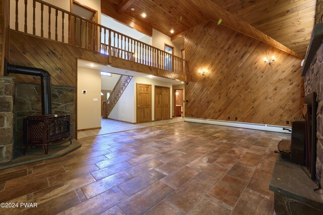 unfurnished living room with a high ceiling, a wood stove, wood walls, and wood ceiling