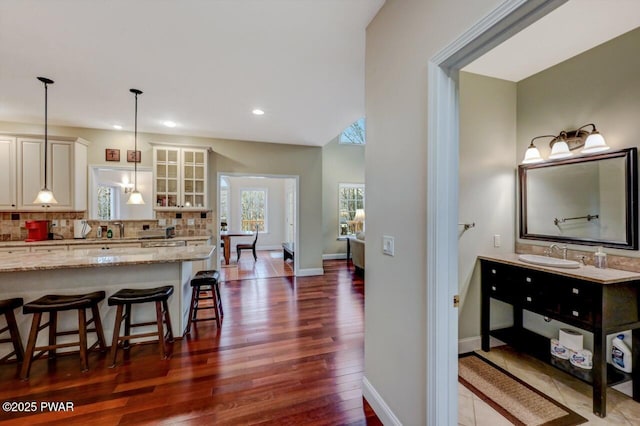 kitchen featuring light stone counters, decorative backsplash, glass insert cabinets, a sink, and a kitchen bar